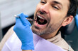 © Home-stock - Man patient sitting in dental chair while dentist examining his teeth using dental tools, male receiving dental checkup and treatment