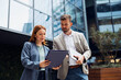 © Novak - Businesswoman showing a document to her male colleague in front of a modern office building.