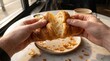 © Omishu Makes - Two hands gently breaking apart a fresh, warm, flaky baked croissant showing its buttery interior.
