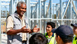 © SERHII - A smiling construction mentor teaching a group of young apprentices on a building site. Vocational education and skilled trades