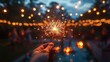 © smalltinykid - hand holding a glowing sparkler at dusk with warm string lights, blurred friends and a fire pit in the background, festive and joyful atmosphere