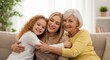 © SHALENA - Three generations of women hugging and smiling on a couch together