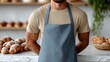 © Nataliia_Trushchenko - Male baker wearing a beige shirt and blue apron stands behind a marble countertop with various baked goods displayed in a bright, modern bakery setting