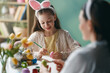 © Konstantin Yuganov - Smiling Girl with Bunny Ears Painting Easter Eggs with Mother at Home