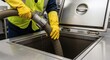 © ramenguy - Person in yellow gloves cleaning a commercial kitchen grease trap using an industrial vacuum hose.