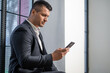 © zinkevych - Male focused on smartphone while posing in modern workplace