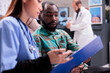 © DC Studio - Close up of african american man reviewing medical records along with asian female member of in house hospital staff. Doctor indicating treatment to young male patient at sanatorium lobby.