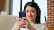 © DC Studio - Cheerful girl texting friend on touchscreen phone while working remotely. Cheerful woman sending messages on mobile phone while listening to music and doing work from home. Handheld shot