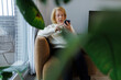 © Westend61 - Senior sitting in armchair using phone in cozy living room with plants