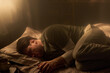 © Mediaphotos - Man lying on bed curled up on side appearing to sleep or rest with head on pillow hands near face soft light coming through window