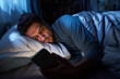 © Mediaphotos - Young man lying in bed using smartphone at night, illuminated by screen light, holding device in hand, appearing tired while looking at phone in dark bedroom