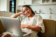 © Marko Geber - Smiling woman using laptop on sofa at home