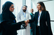© oneinchpunch - Diverse businesswomen shaking hands during corporate meeting in dubai