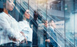 © alphaspirit - People stand in a line at an office building during the day with glass reflections showing their serious expressions and surroundings