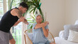 © luciano - Active elderly woman exercising inside home with a personal trainer stretching exercises for shoulders and arms in a modern living room. Healthy  lifestyle, strength training, and wellness concept
