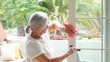 © luciano - Elderly woman with glasses cleaning a glass door with a pink cloth in a bright modern home interior, representing household chores and everyday domestic life