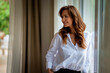 © sepy - Smiling brunette haired woman standing at floor-to-ceiling window in a modern interior