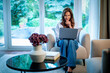© sepy - Portrait of an elegant woman with her laptop relaxing in an armchair in her bright, minimalist home