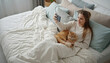 © Guillotine - Woman sitting on bed and taking selfie with cat in cozy bedroom