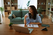 © djile - Young woman smiling while working from home holding a glass of water at her desk