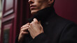 © A2Z AI  - Serious young adult in a formal black coat with an upturned collar, adjust clothing outdoors against a deep red building, close up, partial view
