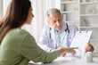 © Anastasiya - Senior male doctor explaining medical document and treatment plan to female patient during clinic consultation. Healthcare professional reviewing healthcare paperwork