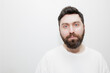 © Timur Abasov - A direct, neutral headshot portrait of a man with dark hair, beard and blue eyes in a white t-shirt on a white background. Stock photo