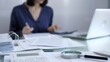 © volha_r - Magnifying glass, white calculator, pen and documents are lying on accountant's desk. Businesswoman wearing blue dress is working with documents on the background. Business and audit concept