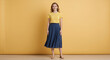 © Vyatcheslav - Smiling young woman standing in studio. Full body portrait of female model in yellow t-shirt and navy blue midi skirt. Casual summer fashion on yellow background