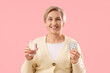 © Pixel-Shot - Mature woman with pills and glass of water experiencing menopause on pink background