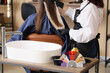 © Pixel-Shot - Hair color palette, spray and sink on table against female hairdresser working with client in beauty salon
