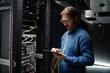 © Seventyfour - Caucasian middle aged man standing in server room operating tablet while holding network cables, focusing on managing data center equipment surrounded by server racks