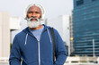 © Wavebreak Media - African american senior man wearing hoodie with bag strap listening on headphones at city square