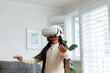 © Wavebreak Media - Girl wearing VR headset reaching forward in well-lit living room with gray sofa and white shutters