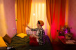 © _KUBE_ - Teen girl in casual clothing sitting on bed in warm sunset room wearing a beanie and playing with a tennis ball. Bored indoor moment and relaxed home atmosphere. Side view