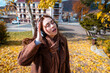 © _KUBE_ - Top view of a Caucasian young woman in a coat listening to music with headphones, singing and dancing in autumn park. Concept of happiness and carefree