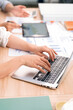 © NAMPIX - Close up of business team hands typing on laptop and analyzing financial data reports on wooden desk in modern office.