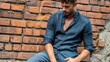 © 4kclips - Urban style and masculine confidence A handsome man poses against a brick wall wearing a denim shirt and jeans a fashion editorial or streetwear campaign A casual attitude in an outdoor setting.