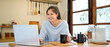 © Stella 16 - Portrait of a young woman using tablet or laptop computer, having online meeting or browsing internet, drinking coffee eating breakfast, drinking drip coffee in the kitchen at home