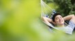 © Your Stock Studio - Smiling asian man relaxing in striped hammock outdoors with hands behind head and eyes closed enjoying peaceful moment in lush green tropical garden