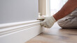 © photo for everything - Professional worker install white baseboard molding to a freshly painted gray wall in a modern renovated room, close up view of the process