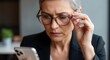 © Eve - Senior business woman in glasses looking closely at smartphone screen with serious concerned expression. Mature female executive checking financial data or reading bad news on mobile.