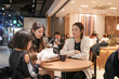 © Masakazu Tokashiki - Three women converse warmly at a cozy cafe table. One smiles brightly, engaging in lively discussion. Soft lighting enhances the intimate, friendly ambiance. Perfect for scenes of friendship
