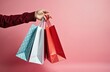 © miss irine - Person holds three shopping bags filled with goods. Red blue and white bags show purchases after retail therapy or gift buying. Simple background provides copy space.