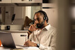 © Tof - Photographie - Portrait d'un jeune homme noir de 30 ans qui travaille à la maison en télétravail. Il est assis devant un ordinateur portable et il a un casque audio sur les oreilles