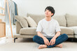 © buritora - A smiling young Asian man sitting in front of the sofa in the living room.