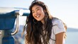 © Iryna - Asian female young adult laughing by seaside viewer scope wearing white tee and hoop earrings sunlit beach portrait carefree joyful traveler
