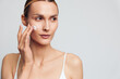 © SHOTPRIME STUDIO - Young woman applying face cream on clean skin, skincare routine, natural beauty, soft lighting, white background, focused expression, casual wear, healthy lifestyle concept