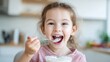 © Iuliia - Little girl eating yogurt with spoon in kitchen. Happy child enjoying healthy dairy snack. Breakfast domestic scene and nutrition concept for children development and family meal time.