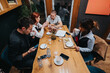 © qunica.com - Four people share coffee and conversation around a wooden table in a cozy cafe. A casual winter business gathering among friends with notes and devices.